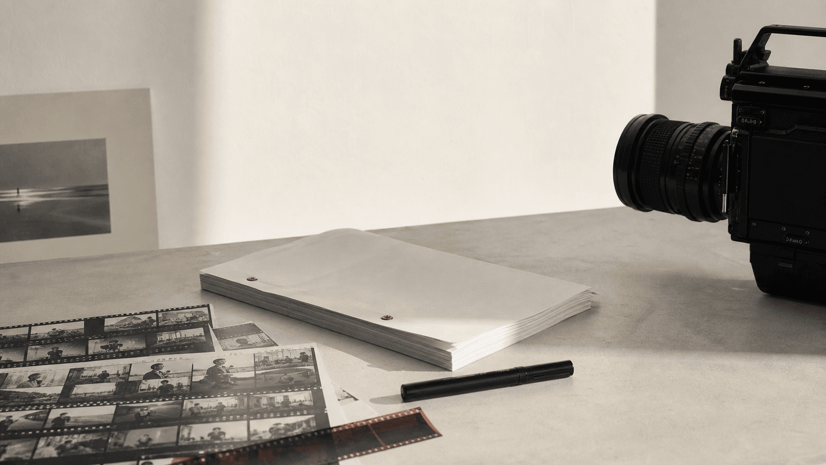 A restrained studio still life with camera, screenplay, and contact sheets